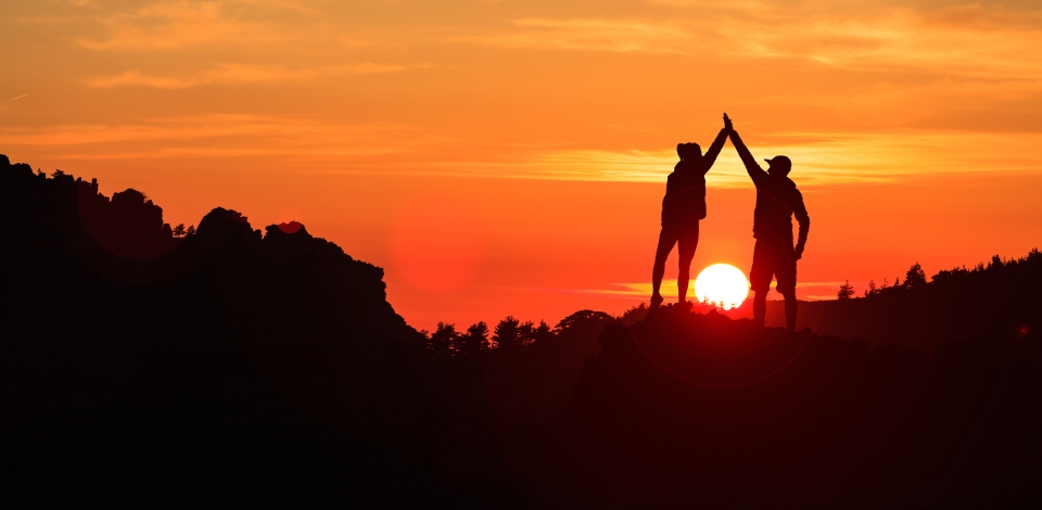 Teamwork couple celebrating in inspiring mountains sunset