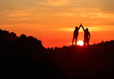 Teamwork couple celebrating in inspiring mountains sunset